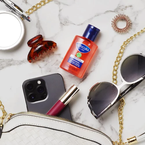 Cuticura Original Floral & Fruity hand gel by handbag next to a phone and sunglasses
