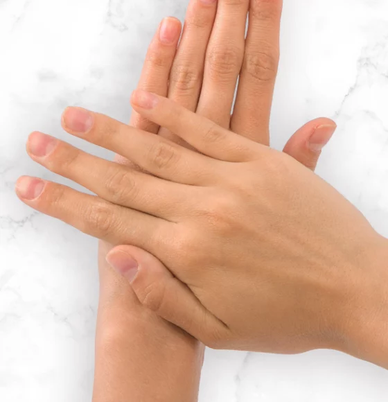 A close up of a pair of hands with smooth looking skin placed on a marble surface.